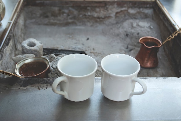 Kawa po turecku na węgiel drzewny. Kawa jest przygotowywana na węglach w tureckiej cezve kawowej. Dwie filiżanki stoją na powierzchni w pobliżu węgli.