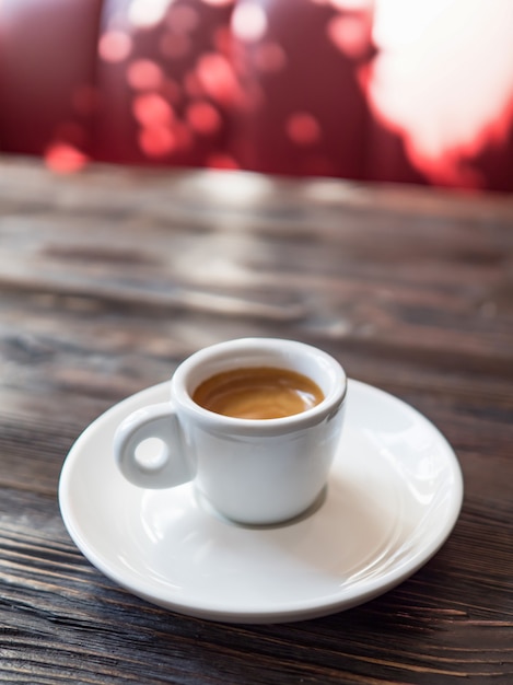 Kawa w białej filiżance stoi na drewnianym stole. Piękny minimalistyczny widok z filiżanką kawy w słonecznej kawiarni.