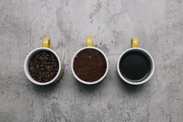 Kawa w proszku, fasola i napój ustawione na każdym kubku na szarym tle.