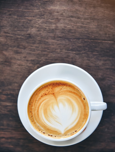 Kawa z kremem w kształcie serca, biała filiżanka na stole drewna.