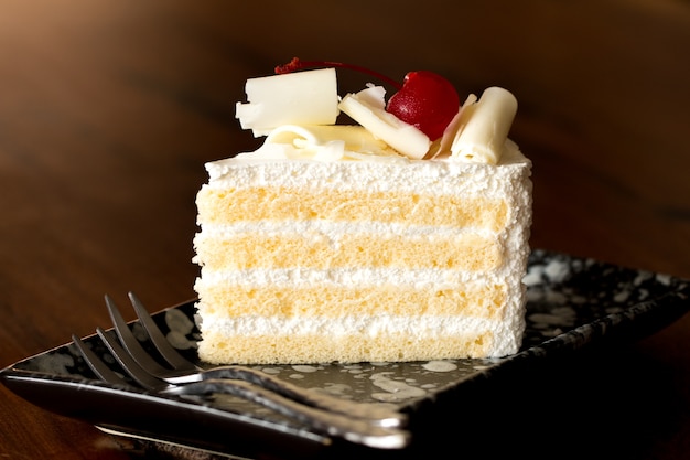 Kawałek białego tortu z lodem waniliowym i wiśniową, zwieńczoną białym serem