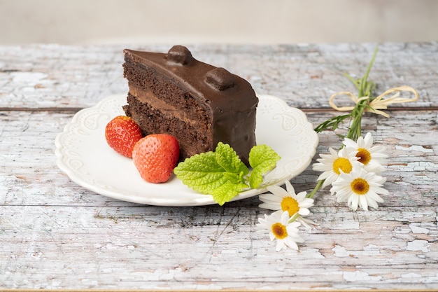 Kawałek ciasta czekoladowego na białym talerzu vintage z kwiatami stokrotki z boku na drewnianym stole