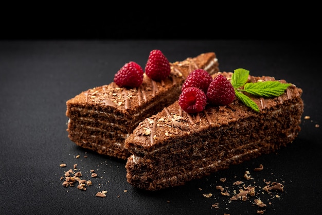 Kawałek ciasta czekoladowego z nadzieniem mlecznym i malinami na czarnej powierzchni.