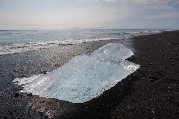 Kawałek góry lodowej na czarnej piaszczystej plaży błyszczący ocean w tle blisko