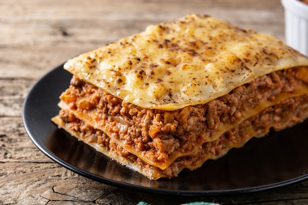 Kawałek mięsa lasagne na czarnym talerzu na drewnianym stole