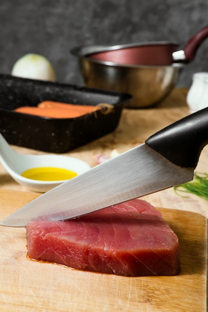Zdjęcie kawałek mięsa z tuńczyka na desce i ręcznie krojąc go nożem