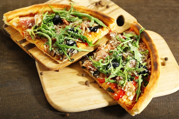 Kawałek pizzy z rukolą na desce do krojenia na kolorowym drewnianym tle
