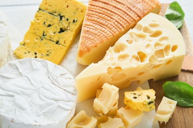 Kawałek sera maasdam i wędzony ser camembert ser pleśniowy parmezan ser brie z bazylią i pieprzem na białej marmurowej desce białe drewniane stare tło Zestaw lub asortyment serów Widok z góry