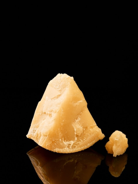 Kawałek twardego sera z bliska, selektywne focus. Parmigiano odbija się na ciemnym stole.
