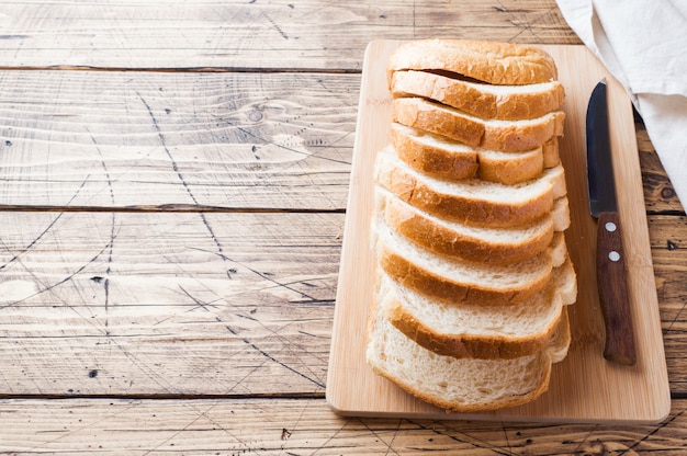Kawałki bochenka białego chleba na grzance na drewnianym stole.