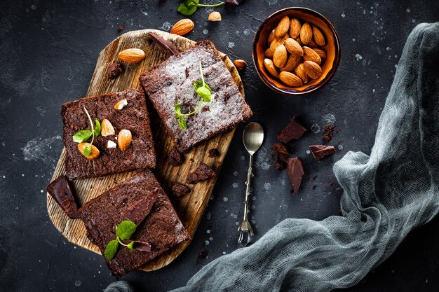 Kawałki domowej roboty brownie czekoladowe z liśćmi mięty i orzechami na szarym tle, widok z góry