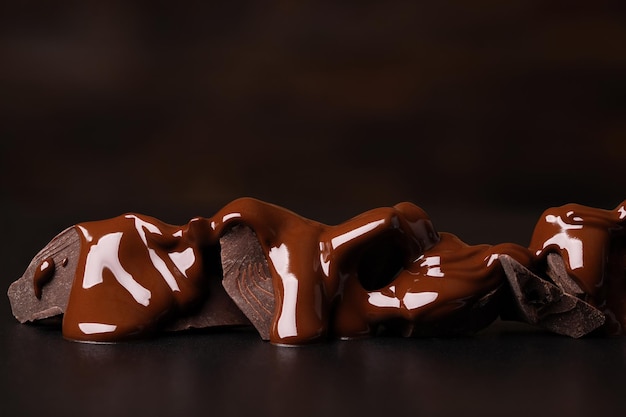 Kawałki gorzkiej czekolady pokryte roztopionym kakao na czarnym stole słodki deser