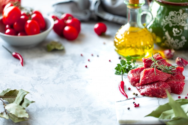 Kawałki posiekanego surowego świeżego mięsa filet na białym tle z marmuru. Pomidory, papryka chili i zioła do gotowania. Skopiuj miejsce