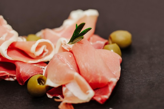 Kawałki prosciutto szynki suszonej wieprzowiny z oliwkami na czarnej tablicy