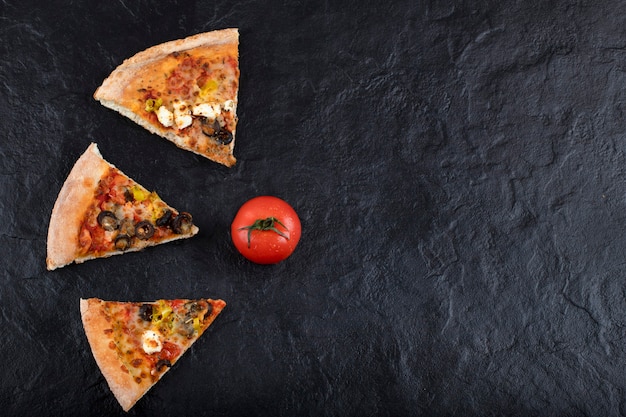 Kawałki pysznej pizzy ze świeżych czerwonych pomidorów umieszczone na czarnym tle.