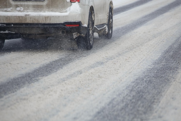 Kawałki śniegu spływają z kół brudnego białego samochodu poruszającego się szybko w świetle dziennym z selektywnym skupieniem