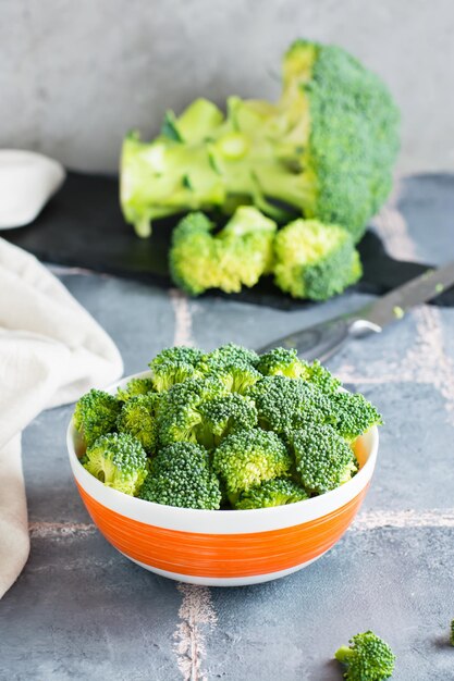 Kawałki surowych brokułów w misce i nóż na stole Gotowanie zdrowego wegetariańskiego jedzenia Widok pionowy Zbliżenie