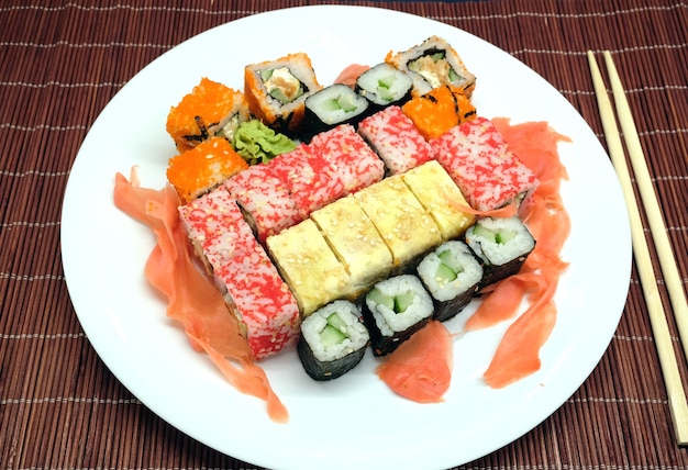 Kawałki sushi na białej tablicy i dwa pałeczki nad brązowym wiklinowym mata słomy widok z góry bliska