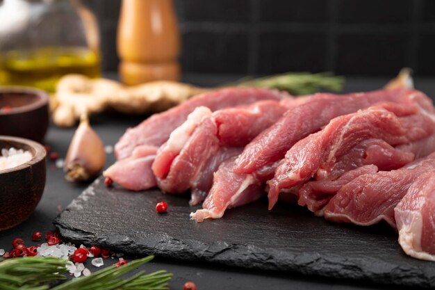 Kawałki świeżego mięsa wieprzowego na czarnym stole, blisko surowe mięso z przyprawami do gotowania