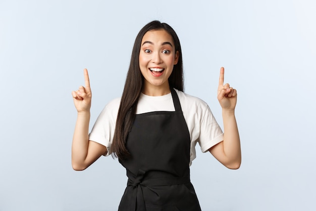 Kawiarnia, Mały Biznes I Koncepcja Uruchamiania. Personel Restauracji W Czarnym Fartuchu Pokazujący Najlepsze Promo. Wesoła Młoda Koreańska Baristka Zapraszająca Do Kawiarni, Wskazująca Palcami W Górę I Uśmiechnięta