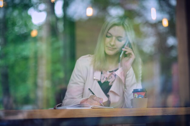 Kawiarnia miejska styl życia kobieta na telefon pije kawę rozmawiając na aplikacji smartfona siedzi w pomieszczeniu w modnej kawiarni miejskiej w odcieniu vintage