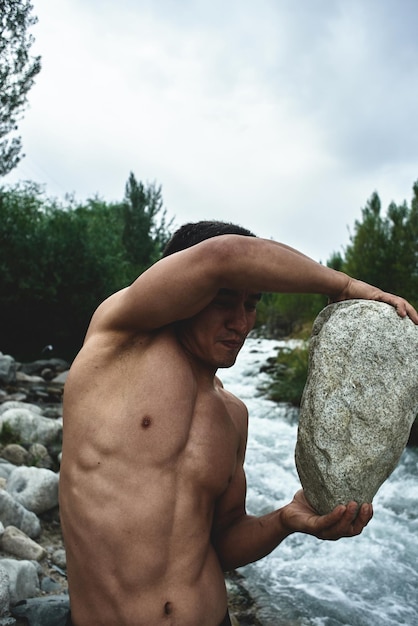 Kazachski muskularny mężczyzna trenuje i ćwiczy nad rzeką w przyrodzie. Azjatycki przystojny robi ekstremalne treningi fitness na świeżym powietrzu