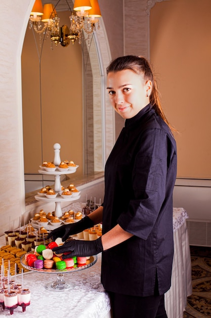 Kelner obsługujący słodki stół cateringowy w hotelu Stoisko z kolorowymi makaronikami ptysiowymi i innymi deserami na imprezę