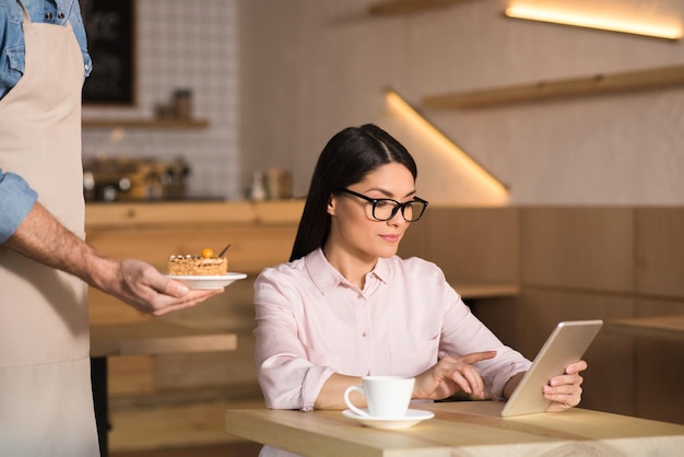 Kelner serwujący ciasto dla bizneswoman za pomocą cyfrowego tabletu w kawiarni