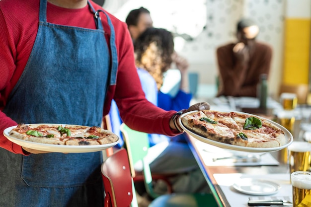 Kelner serwujący pyszną pizzę w przytulnej pizzerii Włoska pizza we włoskiej restauracji Ręce kelnera trzymającego dwie pizze Margherita Oryginalny przepis włoskiej smacznej pizzy margherita