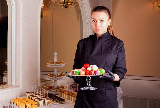 Kelner serwuje przy słodkim stole stoisko z kolorowymi makaronikami Serwis cateringowy