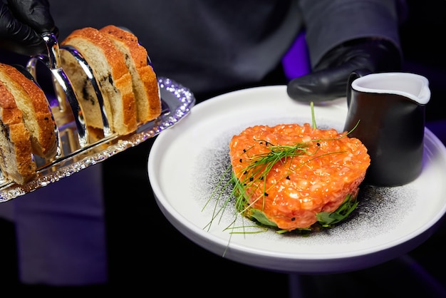 Kelner trzyma tatar z łososia z awokado na białym talerzu w restauracji