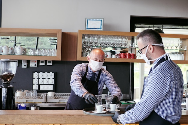 Kelner w medycznej masce ochronnej serwuje kawę w restauracji podczas pandemii koronawirusa reprezentującego nową normalną koncepcję