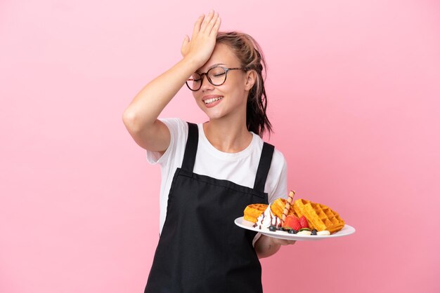 Kelner w restauracji Rosyjska dziewczyna trzymająca gofry odizolowane na różowym tle zdała sobie sprawę z czegoś i zamierza znaleźć rozwiązanie