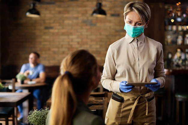 Kelnerka nosząca maskę ochronną podczas przyjmowania zamówienia od klienta w kawiarni