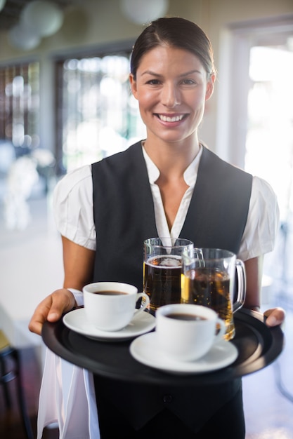 Kelnerka trzyma tacę z filiżanką kawy i kuflem piwa