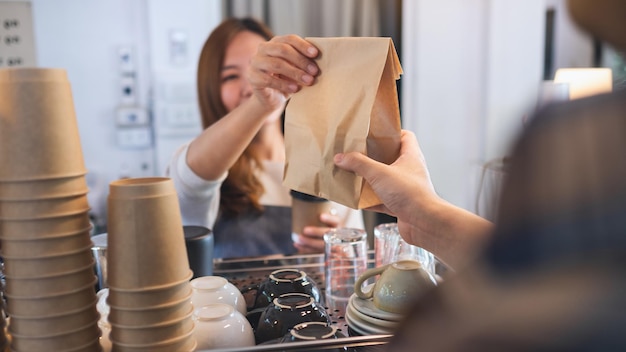Zdjęcie kelnerka trzymająca i serwująca klientom w sklepie kawę i jedzenie na wynos w papierowej torbie