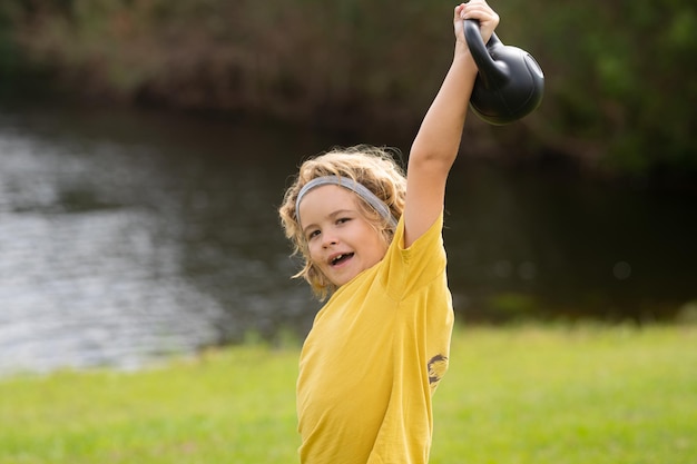 Kid podnoszenia kettlebell w parku na zewnątrz Chłopiec Kid pracy z hantlami Trening sportowy i dzieci