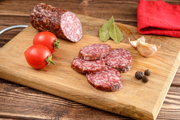 Kiełbasa salami pokrojona w plasterki i pół kiełbasy salami z czosnkiem z liścia laurowego pomidora i pieprzem na desce do krojenia