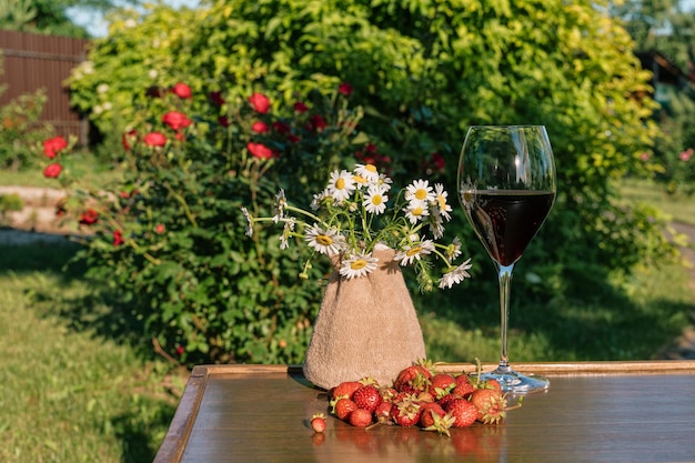 Kieliszek czerwonego wina i truskawek na tle ogrodu na zewnątrz