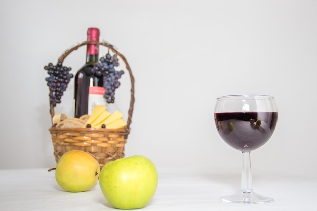 Kieliszek czerwonego wina podawany z żółtymi, zielonymi jabłkami, winogronami i serem w koszyku