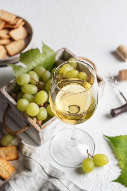 Kieliszek do białego wina martwa natura z winogronami w drewnianym pudełku korkociąg i krakersy na białym tle z teksturą Koncepcja wakacje