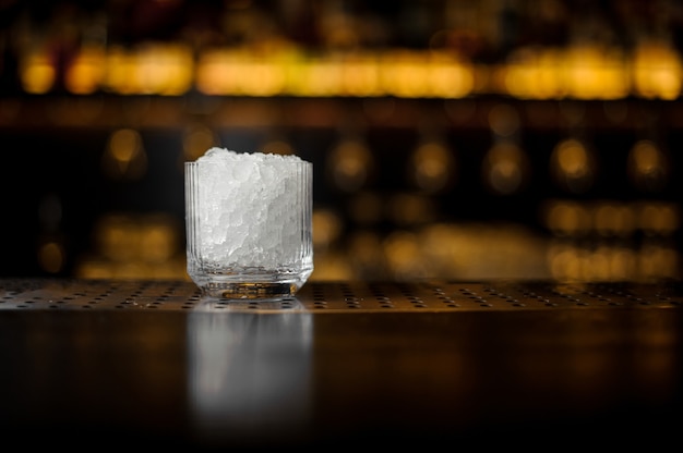 Kieliszek koktajlowy z kostkami lodu na blacie barowym restauracji na niewyraźnym tle świateł