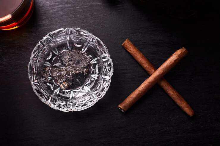 Zdjęcie kieliszek whisky z palącym cygarem.