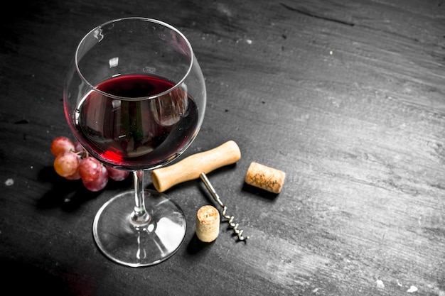 Kieliszek wina żurawia z korkociągiem i gałązką winogron na czarnej tablicy