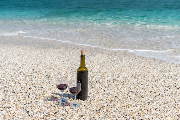 Kieliszki czerwonego wina i butelka na plaży w słoneczny letni dzień