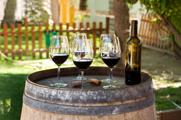 Zdjęcie kieliszki do wina czerwonego i butelka na beczce w ogrodzie