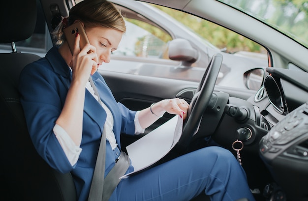 Kierowca jadący drogą, rozmawiający przez telefon, jednocześnie pracujący z dokumentami. Bizneswoman robi wiele zadaniom. Wielozadaniowość przedsiębiorca.