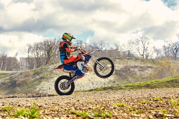 Kierowca motocrossu w akcji, przyspieszający motocykl startuje i wskakuje na trampolinę na torze wyścigowym