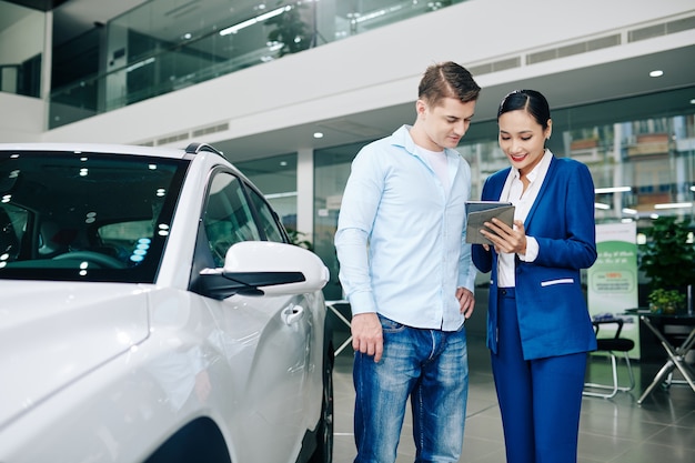 Kierownik sprzedaży pokazujący specyfikacje nowego samochodu w artykule na tablecie