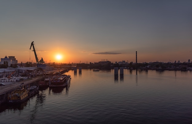 Kijów, Ukraina - 30 maja 2018: Przemysłowa dzielnica Kijowa w dzielnicy Podil. Dniepr i port rzeczny. Widok z mostu wantowego Rybalsky wieczorem podczas zachodu słońca